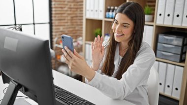 Genç, güzel İspanyol kadın doktor klinikte akıllı telefonuyla video görüşmesi yapıyor.