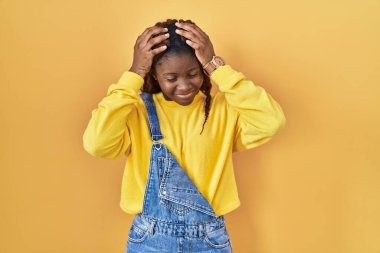 African woman standing over yellow background suffering from headache desperate and stressed because pain and migraine. hands on head. 