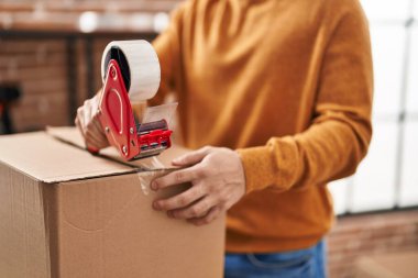 Young hispanic man packing cardboard box at new home
