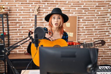 Müzik stüdyosunda klasik gitar çalan beyaz bir kadın korkmuş ve ağzı açık bir şekilde şaşırmış, inançsız bir yüz. 