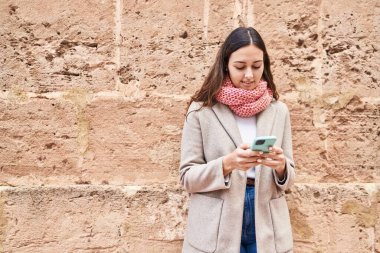 Young beautiful hispanic woman using smartphone wearing scarf at street