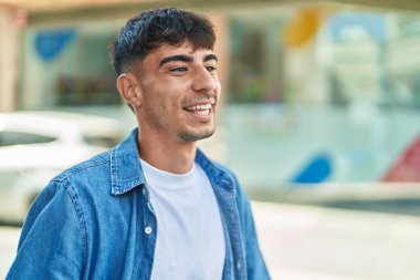 Young hispanic man smiling confident looking to the side at street