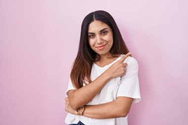 Pembe arka planda duran genç Arap kadın, elini kenarı işaret ediyor. Ciddi ve sakin bir yüz ifadesi sergiliyor. 