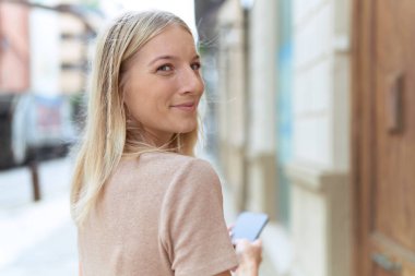 Sokakta akıllı telefon kullanan, kendine güvenen genç sarışın kadın.