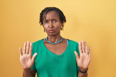 Sarı arka planda duran Afrikalı bir kadın. Avuçlarını hareket ettiriyor. Korkmuş ve iğrenç bir ifadeyle reddediyor. Dur ve yasakla. 