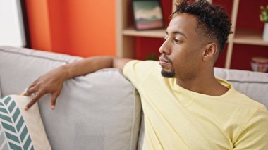 Kanepede oturan Afro-Amerikalı adam ciddi bir ifadeyle oturuyor.