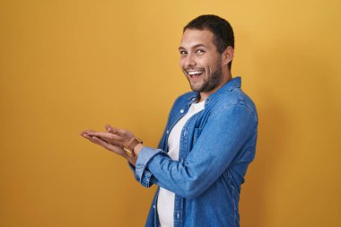 Sarı arka planda dikilen İspanyol adam avuçlarını açıp fotokopi alanını gösteriyor. Reklam sunuyor, mutlu bir gülümseme. 