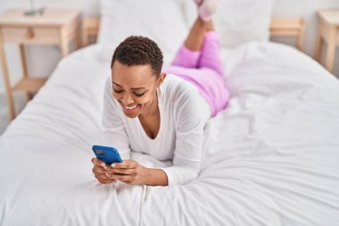 Afrika kökenli Amerikalı bir kadın yatakta akıllı telefon kullanıyor.