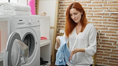 Çamaşır odasında çamaşır yıkayan genç kızıl saçlı kadın.