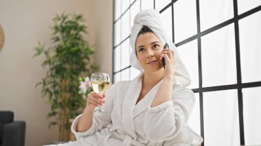 Bornoz giyen, şampanya içen yatak odasında akıllı telefondan konuşan genç, güzel İspanyol kadın.