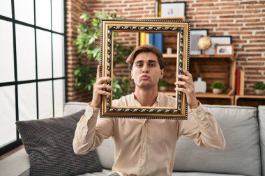 Elinde boş bir çerçeve olan genç bir adam kameraya bakıyor. Öpücük atıyor. Sevimli ve seksi. aşk ifadesi. 