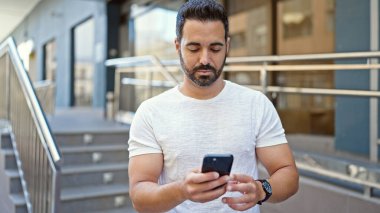 Genç İspanyol adam akıllı telefon kullanıyor. Sokakta ciddi bir ifadesi var.