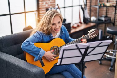 Genç sarışın müzisyen müzik stüdyosunda klasik gitar çalıyor.