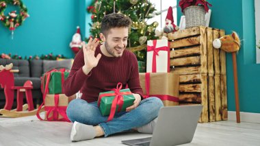 Genç İspanyol adam Noel hediyesini elinde tutarken görüntülü arama yapıyor.