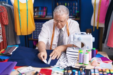 Orta yaşlı, gri saçlı bir adam terzi dükkanında kumaşa iz bırakmış.