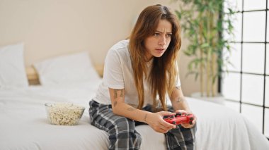 Young beautiful hispanic woman playing video game sitting on bed at bedroom