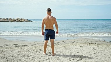 Genç turist arkada durup kumsala bakıyor.