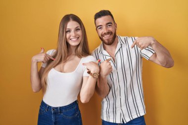 Sarı arka planda duran genç çift, kendine güvenen, yüzünde gülümseme olan, kendini gururlu ve mutlu gösteren bir çift.. 