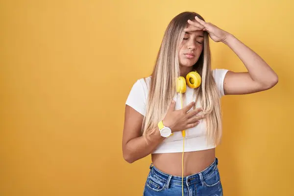 Młoda Blondynka Stojąca Nad Żółtym Tłem Nosząca Słuchawki Dotykające Czoła — Zdjęcie stockowe
