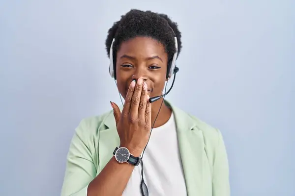 African american woman wearing call center agent headset laughing and embarrassed giggle covering mouth with hands, gossip and scandal concept