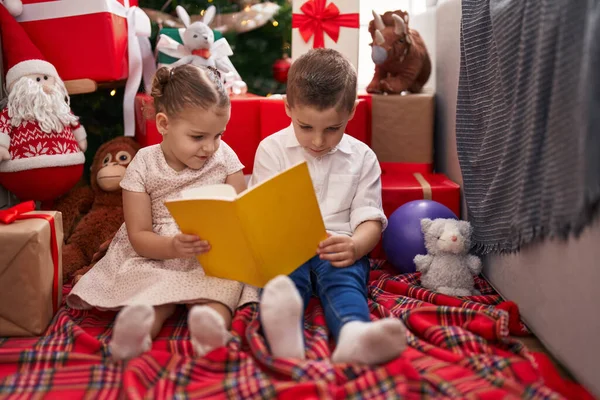 Δύο Παιδιά Διαβάζουν Βιβλίο Κάθεται Στο Πάτωμα Από Χριστουγεννιάτικο Δέντρο — Φωτογραφία Αρχείου