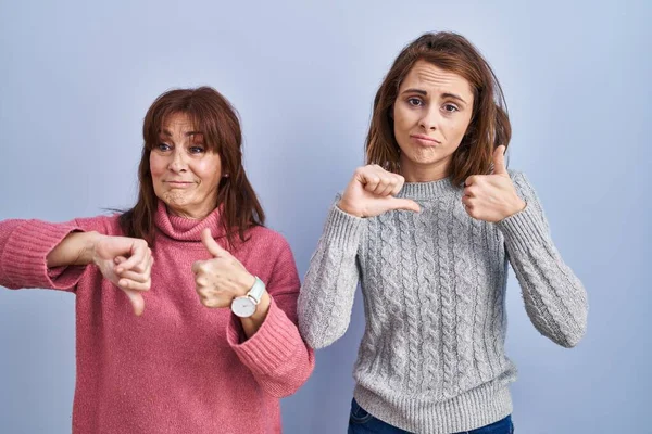 青い背景の上に立っている母と娘は 親指を上下に 意見の相違と合意の表現をしています クレイジーな対立 — ストック写真