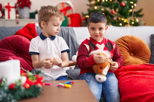 自宅でクリスマスツリーでソファーに座っているおもちゃで遊ぶ2人の子供 — ストック写真