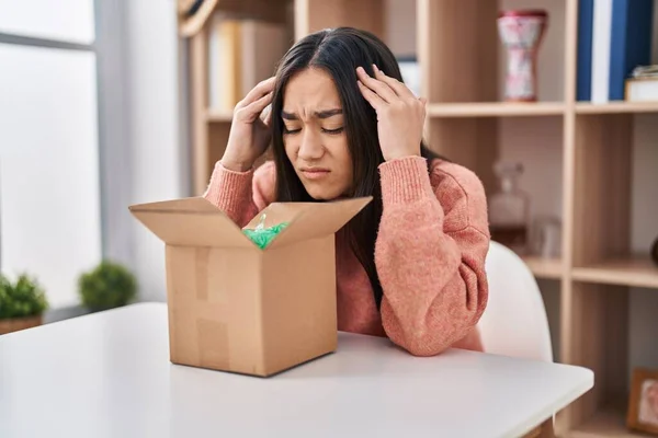 Young south asian woman opening cardboard box with hand on head, headache because stress. suffering migraine.