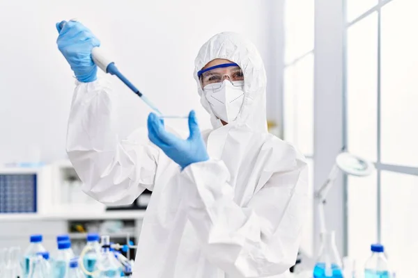 若い金髪女性科学者は 実験室でサンプルに液体を注ぐセキュリティユニフォームを着用しています — ストック写真