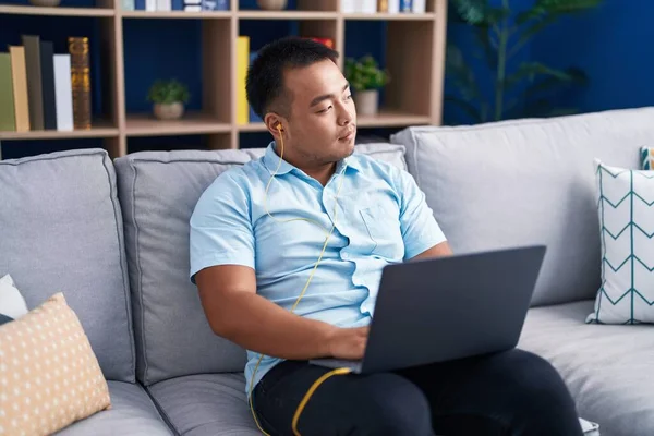 Young Chinese Man Using Laptop Earphones Sitting Sofa Home — Stock Photo, Image