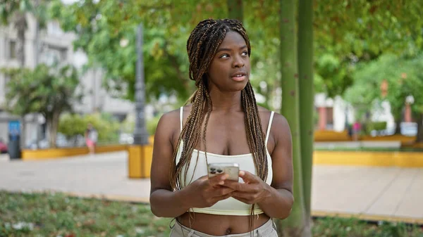 在公园里使用带有严肃表情的智能手机的非洲裔美国女人 — 图库照片