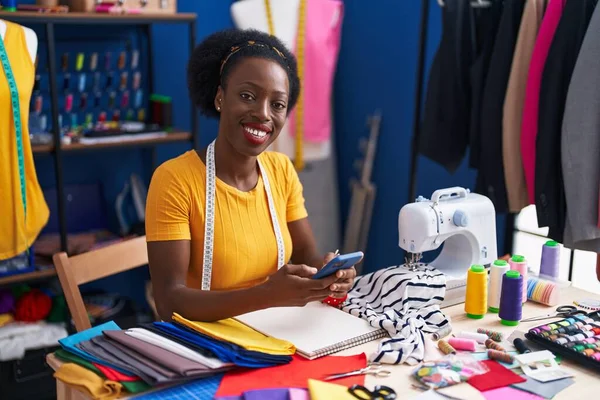 African american woman tailor smiling confident using smartphone at sewing studio