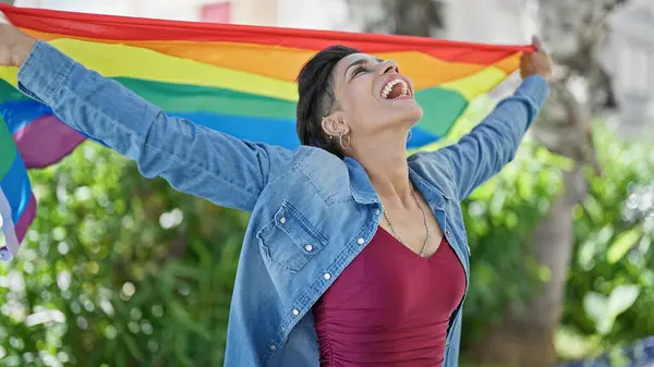 stock image Young beautiful hispanic woman smiling confident holding rainbow flag at park