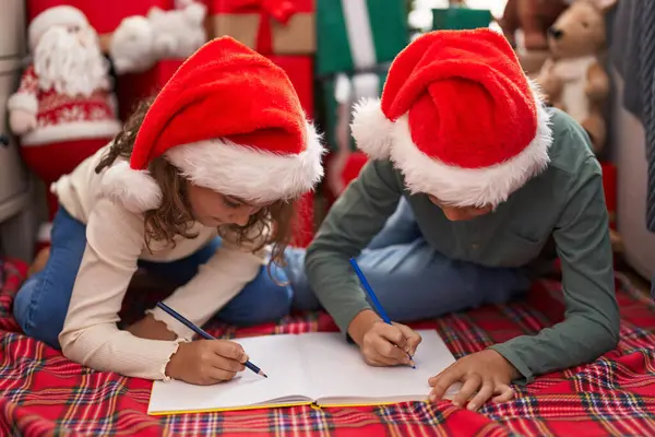 自宅でクリスマスツリーで床に座っているノートに書く2人の子供 — ストック写真
