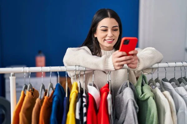 Young Beautiful Hispanic Woman Using Smartphone Leaning Clothes Rack Laundry —  Fotos de Stock