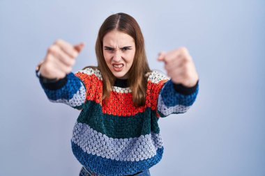 Mavi arka planda öfkeli ve kızgın duran genç İspanyol kız öfkeyle bağırırken kızgın ve öfkeli yumruklar sallıyor. öfke ve agresif konsept. 