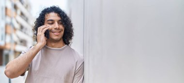 Genç Latin adam gülümsüyor. Kendine güveniyor. Akıllı telefondan konuşuyor.