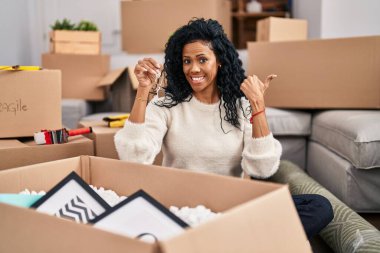 Orta yaşlı, İspanyol bir kadın elinde yeni evin anahtarlarını tutarken baş parmağıyla ağzını açıp gülümsüyor. 