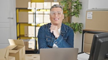 Genç Kafkasyalı iş adamı ofiste gülümseyen dizüstü bilgisayar kullanıyor.