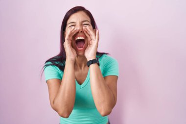 Pembe arka planda duran genç İspanyol kadın elleri ağzında kızgın bir şekilde bağırıyor. 