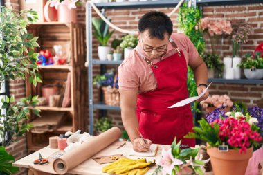 Young chinese man florist writing on notebook reading document at florist