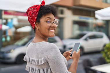 Afro-Amerikalı kadın sokakta akıllı telefon kullanarak kendine güveniyor.