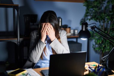 Geceleri ofiste çalışan esmer bir kadın. Ağlarken yüzünü ellerle kapatan üzgün bir ifadeyle. depresyon kavramı. 