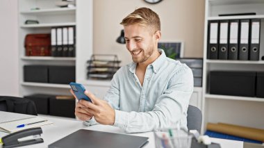 Kafkasyalı genç bir iş adamı ofisteki akıllı telefonu kullanarak işini bitiriyor.