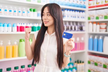 Eczaneden alışveriş yapan genç Çinli bir kadın elinde kredi kartıyla yan tarafı işaret ederek ağzı açık gülümsüyor. 