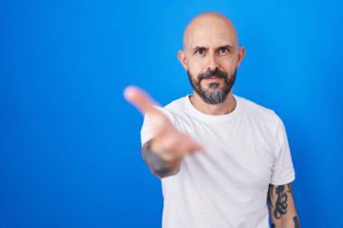 Mavi arka planda dikilen, gülümseyen, yardım eli uzatan ve kabul gören İspanyol dövmeli adam.. 