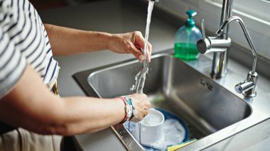 Orta yaşlı İspanyol kadın mutfakta tabak yıkıyor.