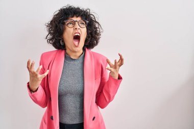 Hispanic woman with curly hair standing over isolated background crazy and mad shouting and yelling with aggressive expression and arms raised. frustration concept. 