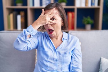 Orta yaşlı İspanyol kadın evinde koltukta oturuyor. Şok olmuş bir şekilde yüzünü ve gözlerini kapatıyor. Utanmış bir ifadeyle parmaklarından bakıyor.. 