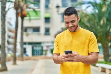 Parkta akıllı telefon kullanarak gülümseyen İspanyol genç adam.